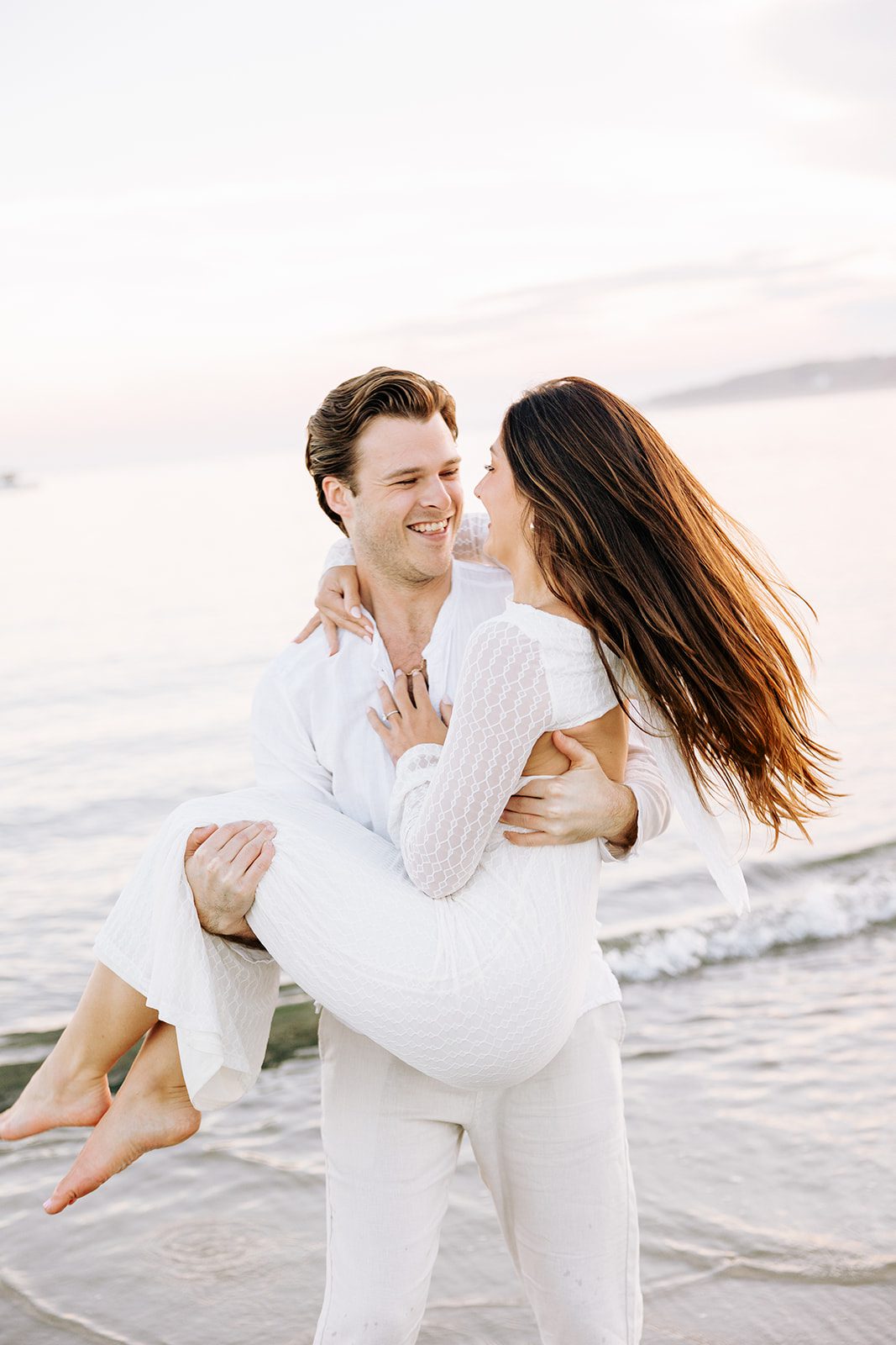 Couple cuddling near rocky shoreline during engagement session at Kettle Cove Maine