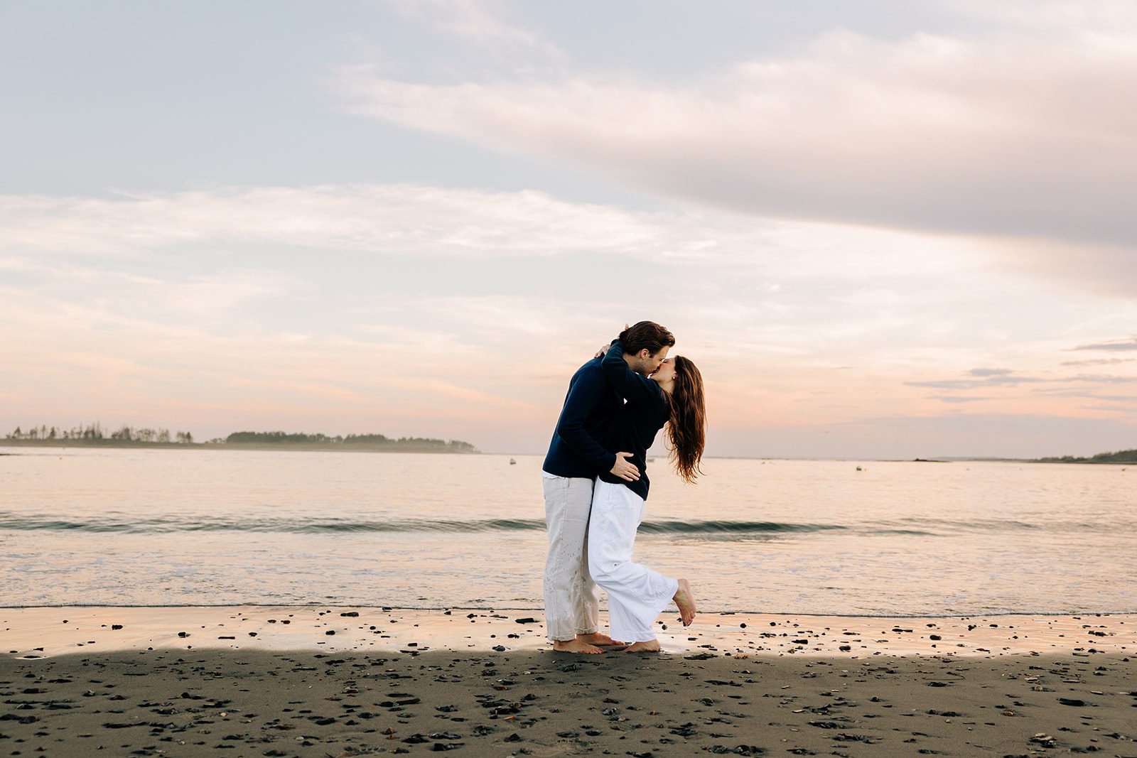 Romantic engagement photo of couple embracing on coastal rocks in Cape Elizabeth Maine at Kettle Cove